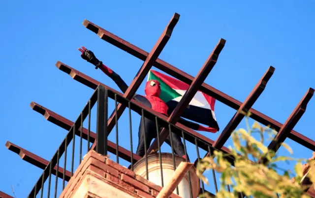 A Sudanese demonstrator dressed as Spiderman waves a national flag from a balcony during a rally in 60 street in the capital Khartoum, on December 6, 2021, to protest a deal that saw the Prime Minister reinstated after his ouster in a military coup in October