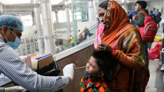 A healthcare worker collects a Covid test swab sample from a boy at a bus terminal in Delhi, India. Photo: 6 December 2021