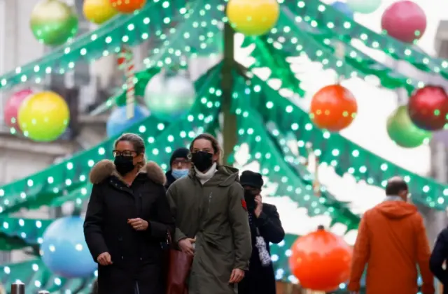 People wearing face masks walk in front of a Christmas tree carousel in Nantes