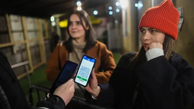 A woman shows her Covid pass to door staff