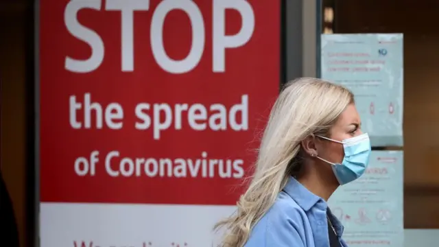 A woman wears a mask as she walks past a sign warning about coronavirus