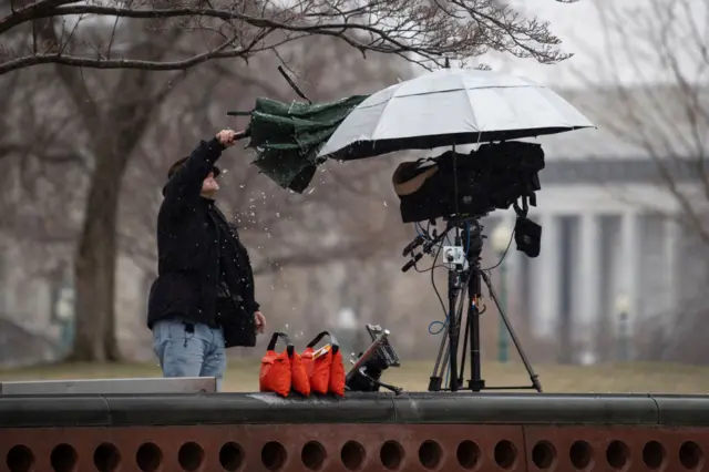 A member of the media brushes ice off umbrella