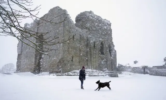 Woman walks dog in snow next to Bowes Castle