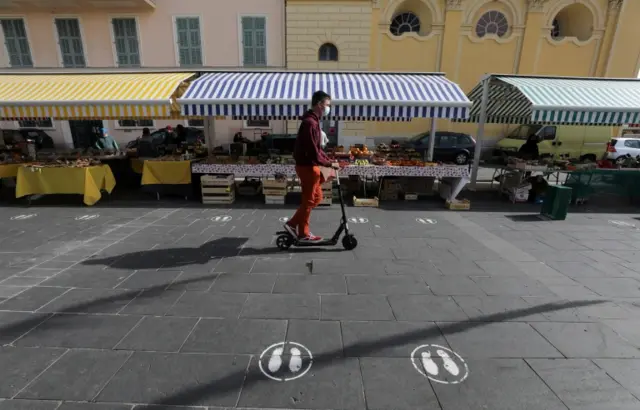 A man, wearing a protective face mask, rides his scooter in a local market in Nice, France