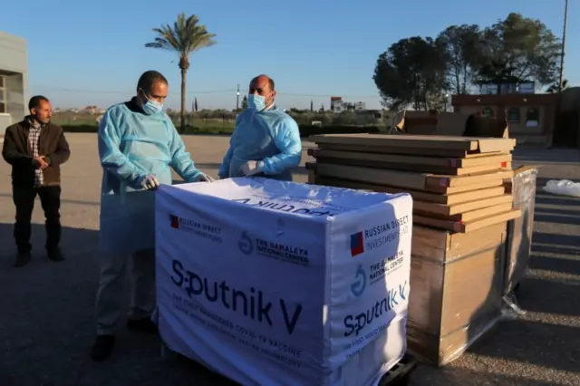 Palestinian health workers stand next to a shipment of Russia's Sputnik V vaccine sent by the United Arab Emirates at the Rafah crossing in the southern Gaza Strip on 21 February 2021
