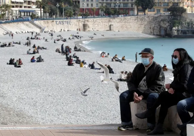 People, wearing protective face masks, sit on the beach of the Promenade des Anglais in Nice, France, on18 February 2021