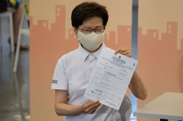 Carrie Lam shows her vaccination record after receiving the jab