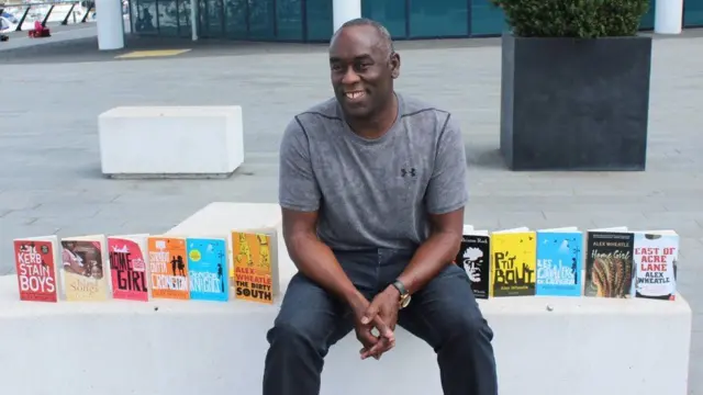 Alex Wheatle sitting beside a row of books