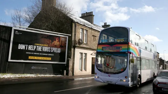 A bus decorated with a rainbow and NHS stickers passes a Coronavirus related advert on a billboard in Falkirk, Central Scotland, where lockdown measures introduced on January 5 for mainland Scotland remain in effect until at least the end of February.