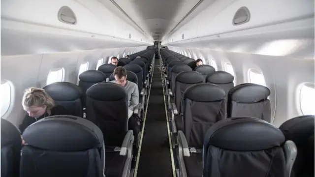 A few passengers sit on seats inside an almost empty plane