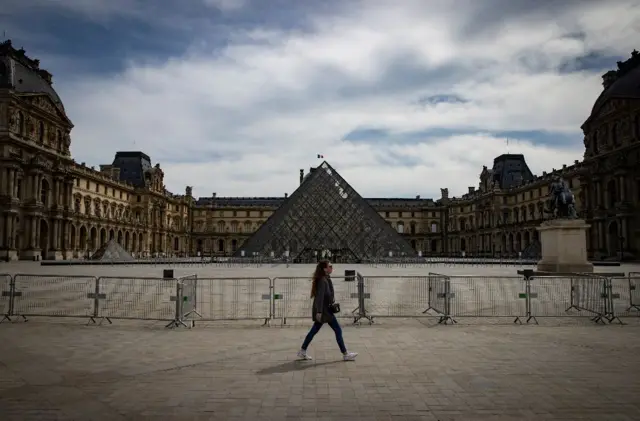 A woman walks infront of the Louvre and its empty courtyard in April 2020