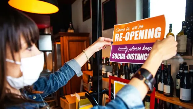 A woman with a sign saying a shop is reopening