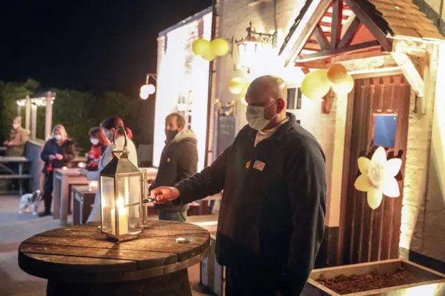 Health care assistant Chellen Chellamboye lights a candle outside the Old House at Home pub in Dormansland, Surrey, during the National Day of Reflection, on the anniversary of the first national lockdown to prevent the spread of coronavirus.