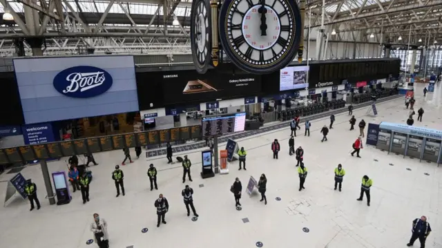 Travellers and workers stand for a minute of silence during the day of reflection to mark the anniversary of Britain"s first coronavirus disease (COVID-19) lockdown, at Waterloo station in London