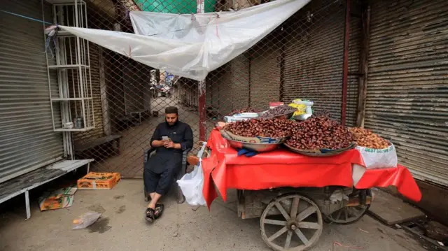 A man sells dates and waits for customers outside a closed market as the government reduces market business hours after new cases of COVID-19 were reported across the country, in Peshawar, Pakistan