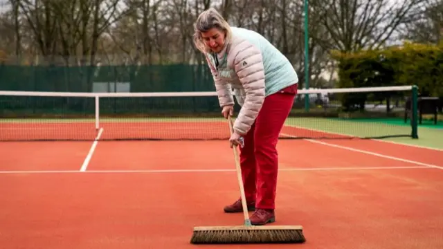 Ruth Williams, welfare officer and ladies captain brushes the courts at Wycombe House Tennis Club in Isleworth, London