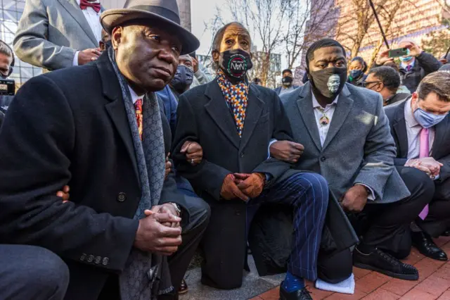 Attorney Ben Crump (L) and Rev. Al Sharpton, the founder and President of National Action Network,(C) and George Floyd's brother kneel outside the Hennepin County Government Center on the opening day of the trial of former Minneapolis police officer Derek Chauvin on March 29, 2021 in Minneapolis, Minnesota.