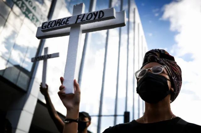 A protester wearing a mask holds a cross with the name of George Floyd during a protest amidst the coronavirus (COVID-19) pandemic at Avenida Presidente Vargas on June 7, 2020 in Rio de Janeiro, Brazil.