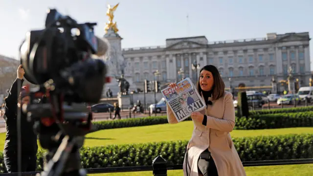 A television journalist holds a copy of a British newspaper as she reports outside of Buckingham Palace in London on January 9, 2020, following the announcement that Britain's Prince Harry, Duke of Sussex and his wife Meghan, Duchess of Sussex, plan to step down as "senior" members of the Royal Family.