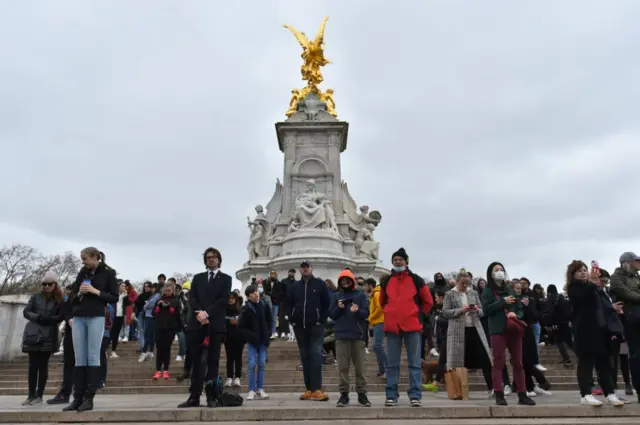 People hold an impromptu silence on the Queen Victoria Memorial outside Buckingham Palace, London, as 41-round Royal gun salutes are fired across the UK