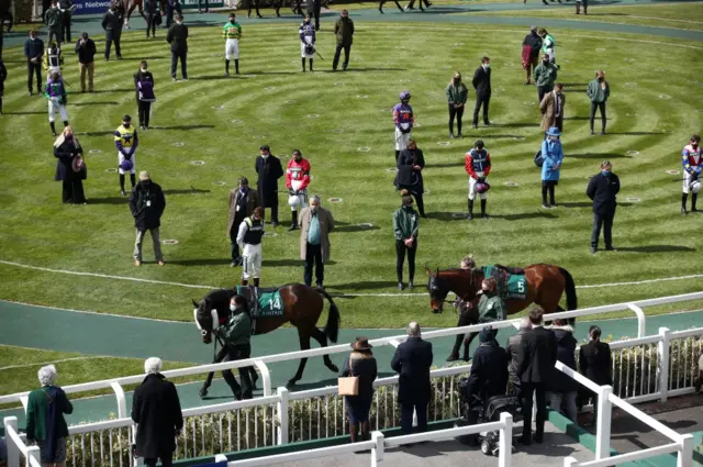 Trainers and jockeys stand in silence in the paddock at Aintree