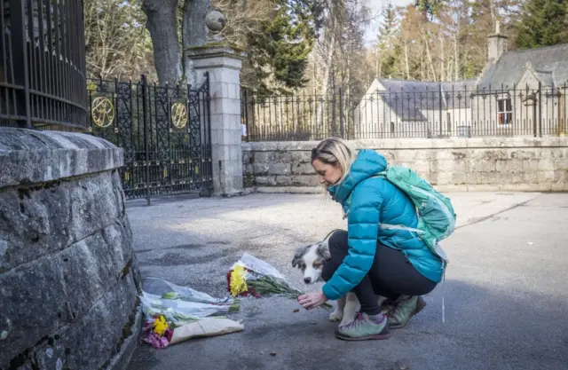 Gayle Cameron, with dog Morlich, lays flowers at the gates of Balmoral Castle in Royal Deeside, Aberdeenshire, following the announcement of the death of the Duke of Edinburgh on 9 April 2021