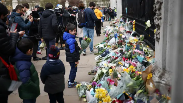 A child brings flowers to a makeshift altar outside Buckingham Palace after Britain"s Prince Philip, husband of Queen Elizabeth, died at the age of 99, in London, Britain