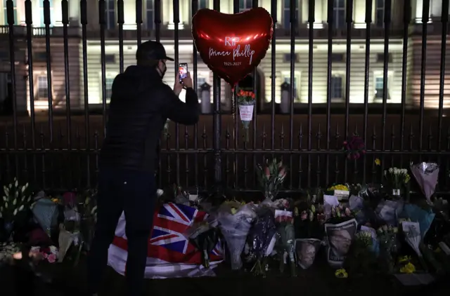 Floral tributes and candles are left outside Buckingham Palace, London, following the announcement of the death of the Duke of Edinburgh at the age of 99.