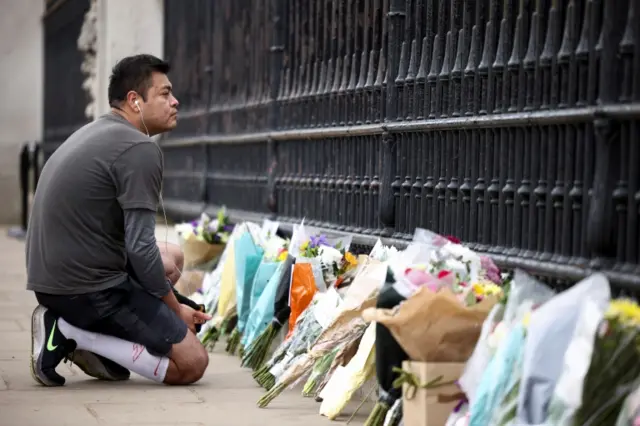 Man next to flowers outside Buckingham Palace