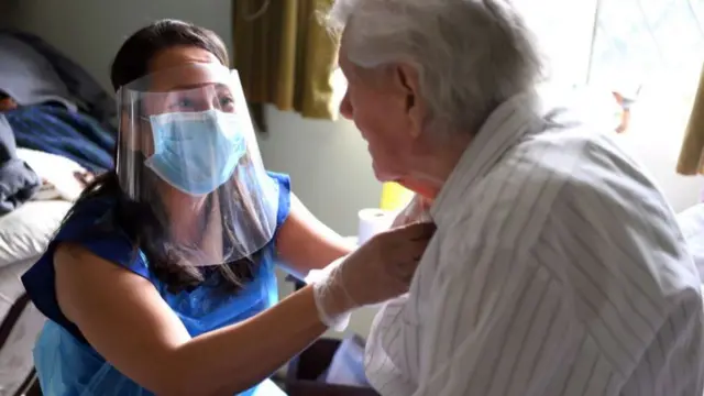 A care worker helping tie an older man's shirt