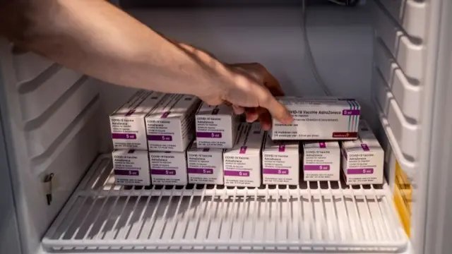 A person reaching into a fridge with boxes of the AstraZeneca Covid vaccine inside