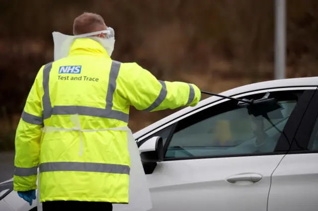 An NHS test and trace staff member giving people a testing kit