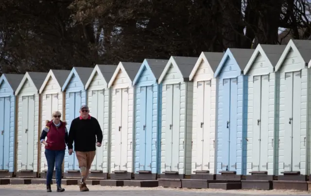 People make their way past beach huts on Avon beach in Mudeford, Dorset.