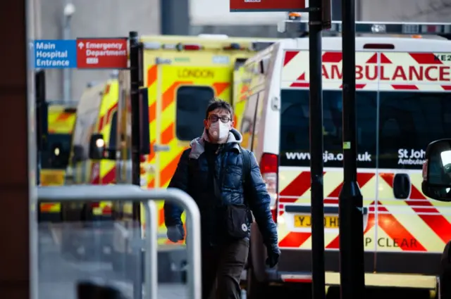 A man in a mask walks past parked ambulances