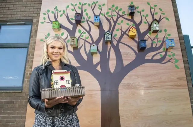 Lottery winner Kate Donaghey holds bird box in front of feature wall