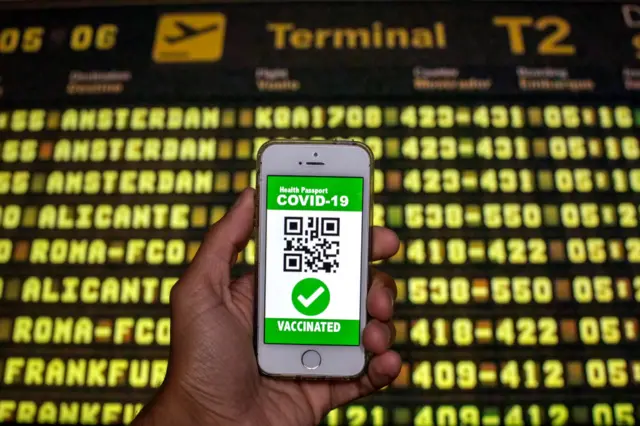 In this photo illustration a symbolic Covid health passport seen displayed on a smartphone screen in front of the flight information panel