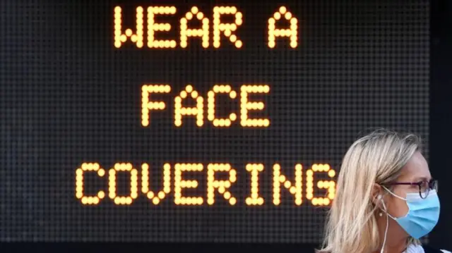 Woman wearing face covering in front of sign saying wear a face covering