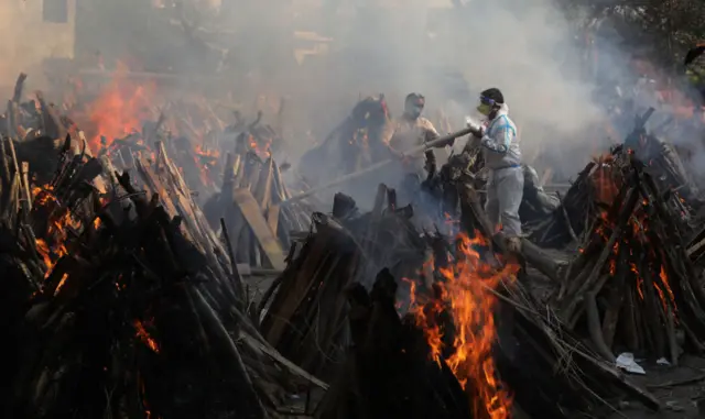 Relatives stand next to burning funeral pyres in New Delhi