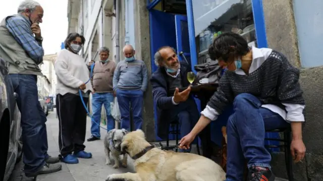 People sit and socialise outside a typical dive bar "Alfredo Portista" as Portugal enters the third phase of easing coronavirus disease (COVID-19) restrictions by allowing clients inside restaurants, bars and cafes, in Porto, Portugal, April 19, 2021