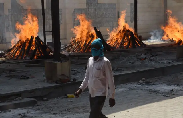 A man walks past multiple funeral pyres of Covid-19 victims