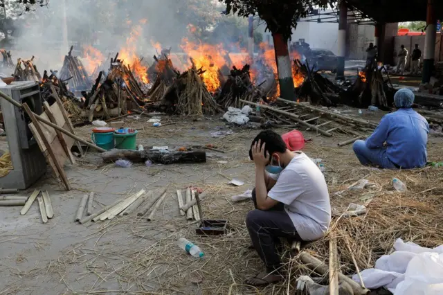 Family members sit next to burning funeral pyres