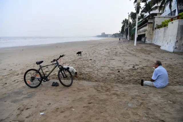 A man sits early in the morning on a deserted beach during restrictions imposed by the state government