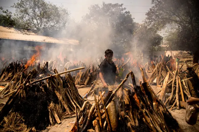 A man performs the last rites of his relative who died of the Covid-19 coronavirus disease as other funeral pyres are seen burning