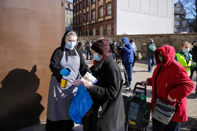 A nun sprays disinfectant on the hands of people waiting in line during the Easter Breakfast for people in need, organised by Caritas in Poznan, Poland, on 4 April 2021