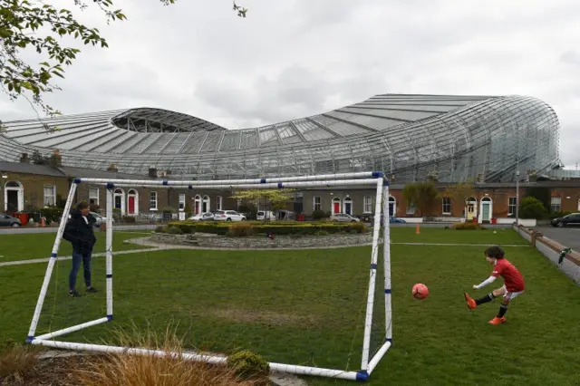 A young fan plays football on a green in Dublin with the Aviva Stadium in the background