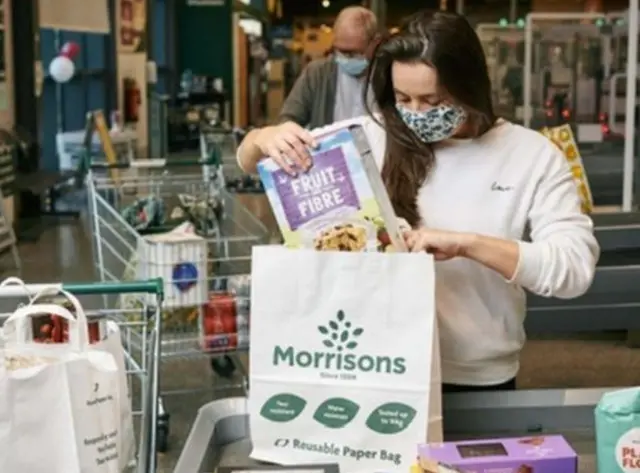 Woman filling paper carrier bag with shopping