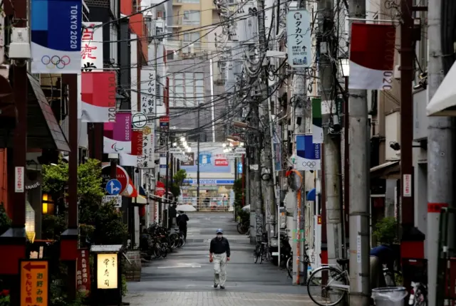 A man wearing a protective face mask walks in a local shopping street decorated with Tokyo 2020 Olympic Games flags