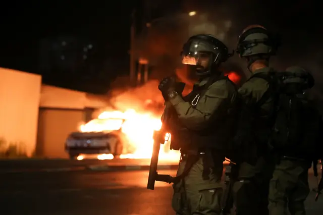 Israeli security forces stand near a burning Israeli police car during clashes between Israeli police and members of the country's Arab minority in the Arab-Jewish town of Lod