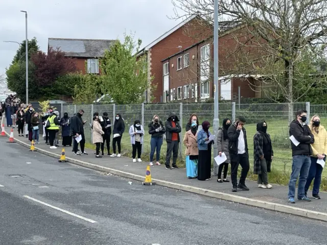 People queue for the vaccination centre at the Essa Academy in Bolton.