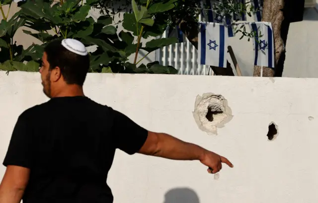 An Israeli man points towards shrapnel holes at the scene of a rocket attack in Ashkelon